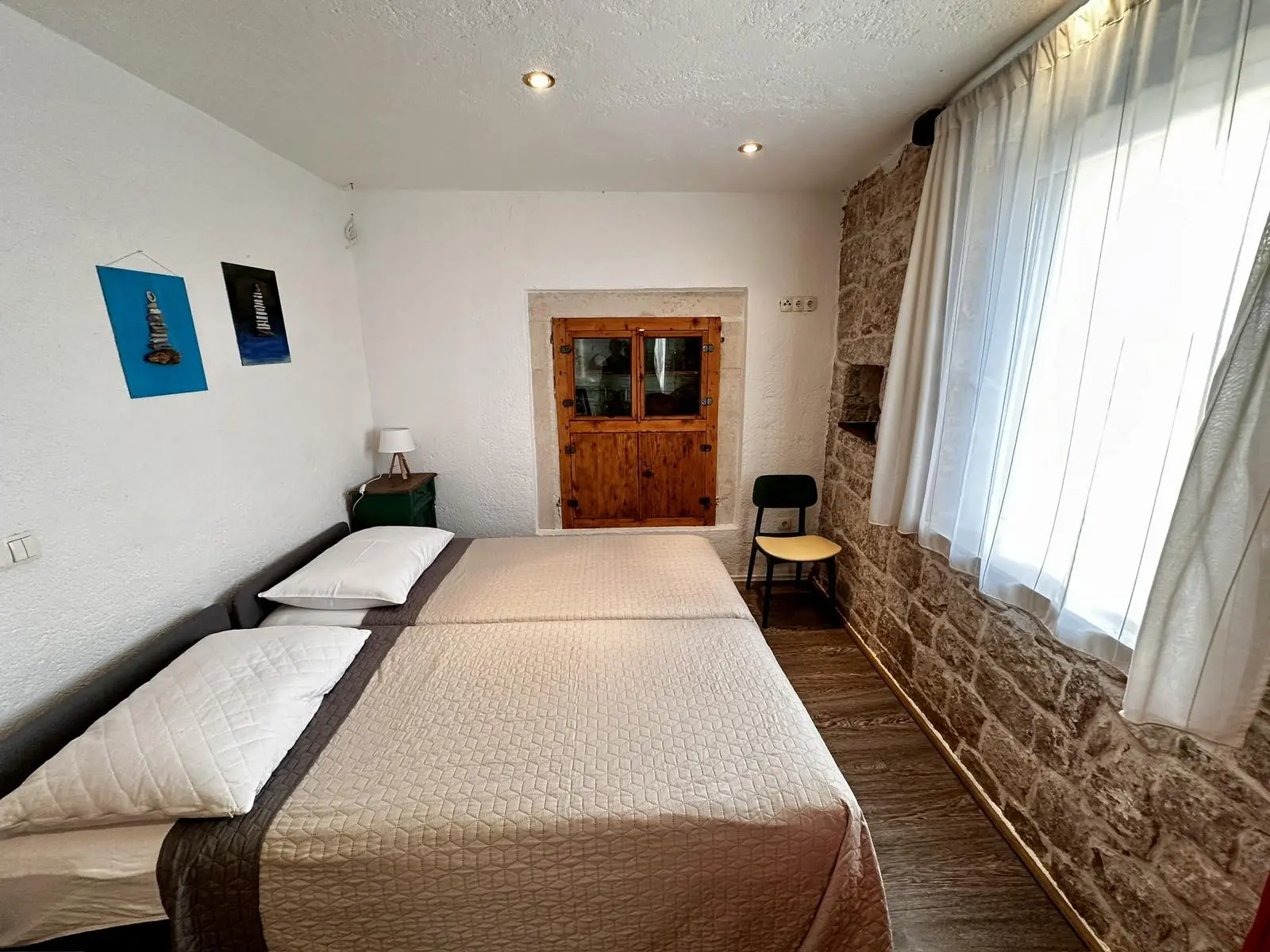 Simple and cozy hotel room with twin beds, white curtains, stone accent wall, and art on the walls.