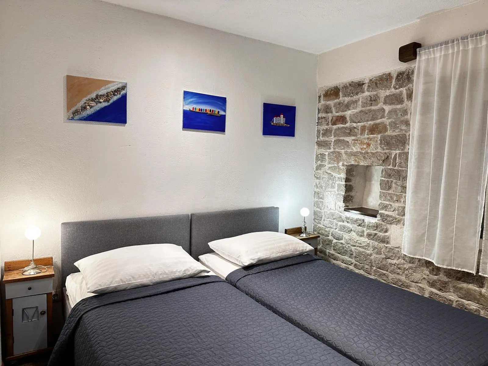 Elegantly appointed twin bedroom with grey bedding, white walls, stone accent features, and marine-themed artwork.