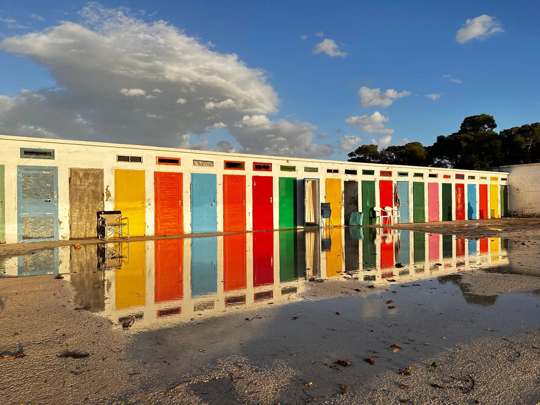 Colorful beach cabins with reflections on the water surface at sunset.