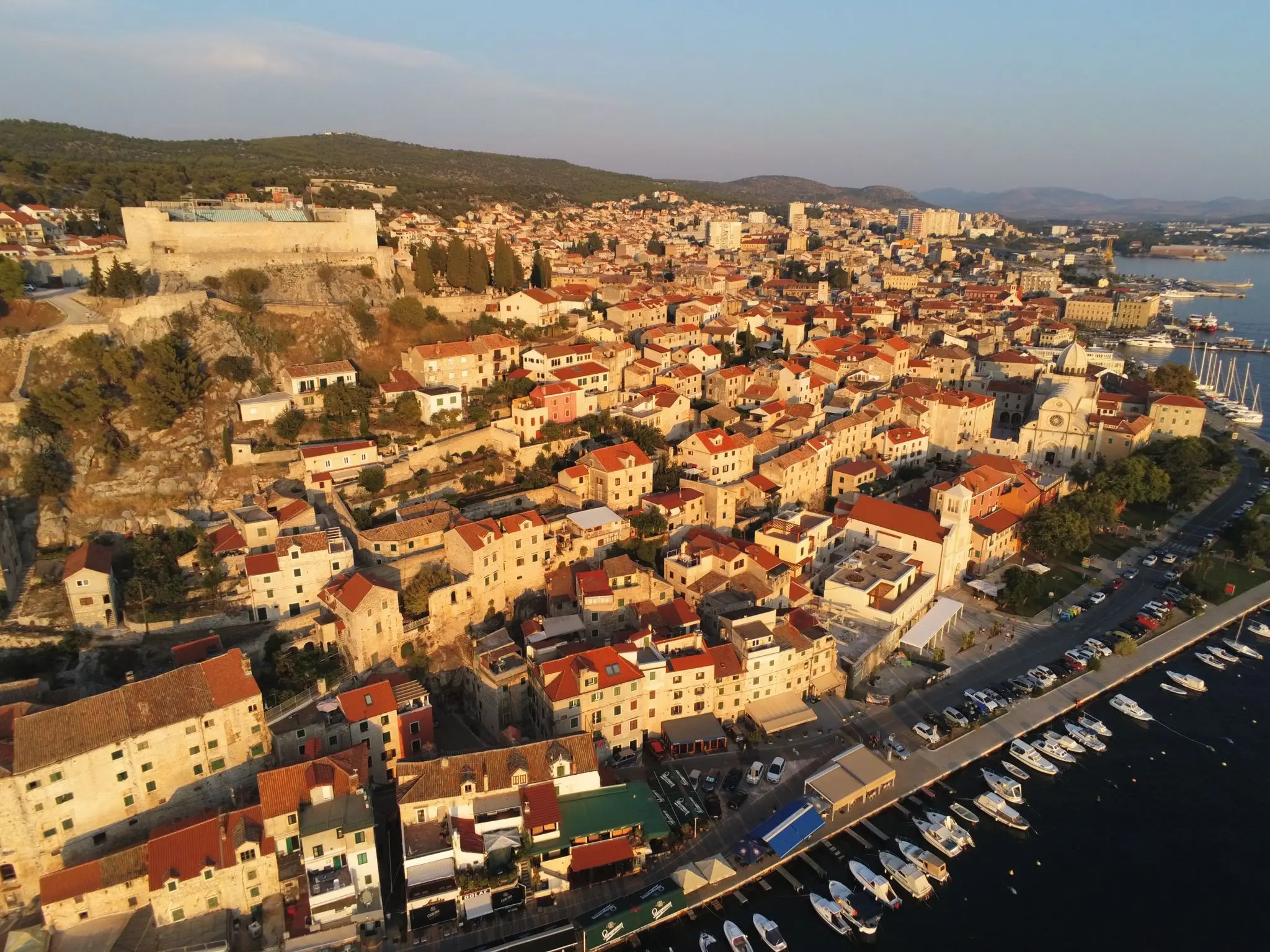 Aerial view of an old coastal town with historic buildings and a marina at sunset.