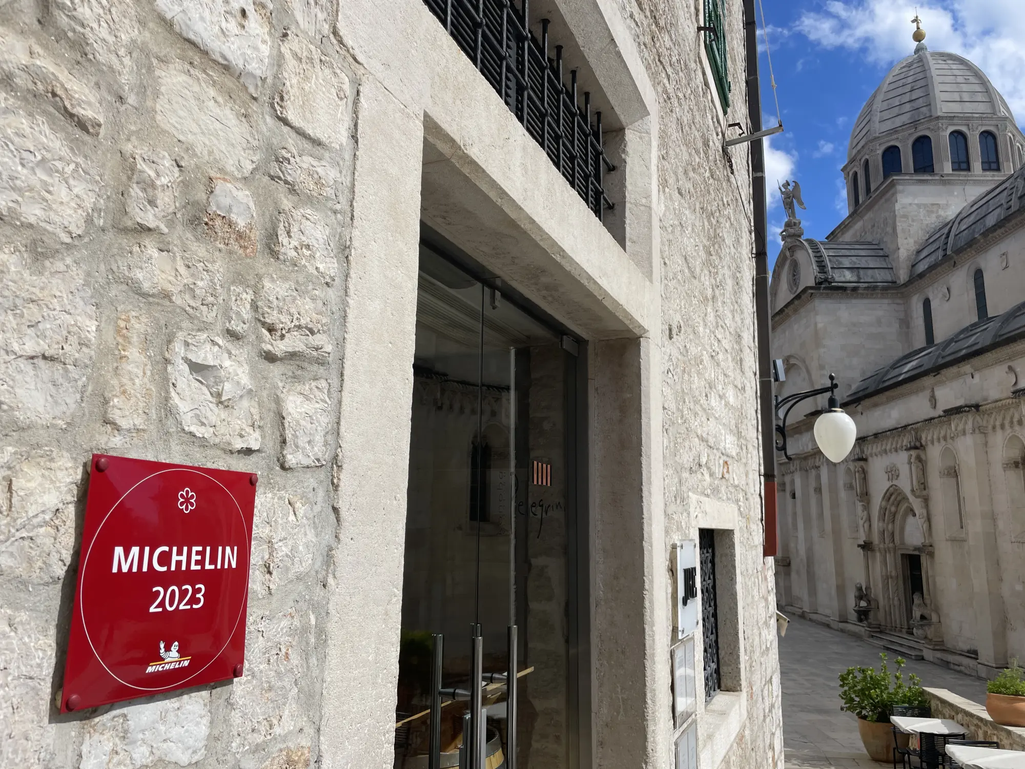 An alley with a Michelin 2023 sign on a stone wall leading to an elegant building with a dome, symbolizing a recognized dining establishment