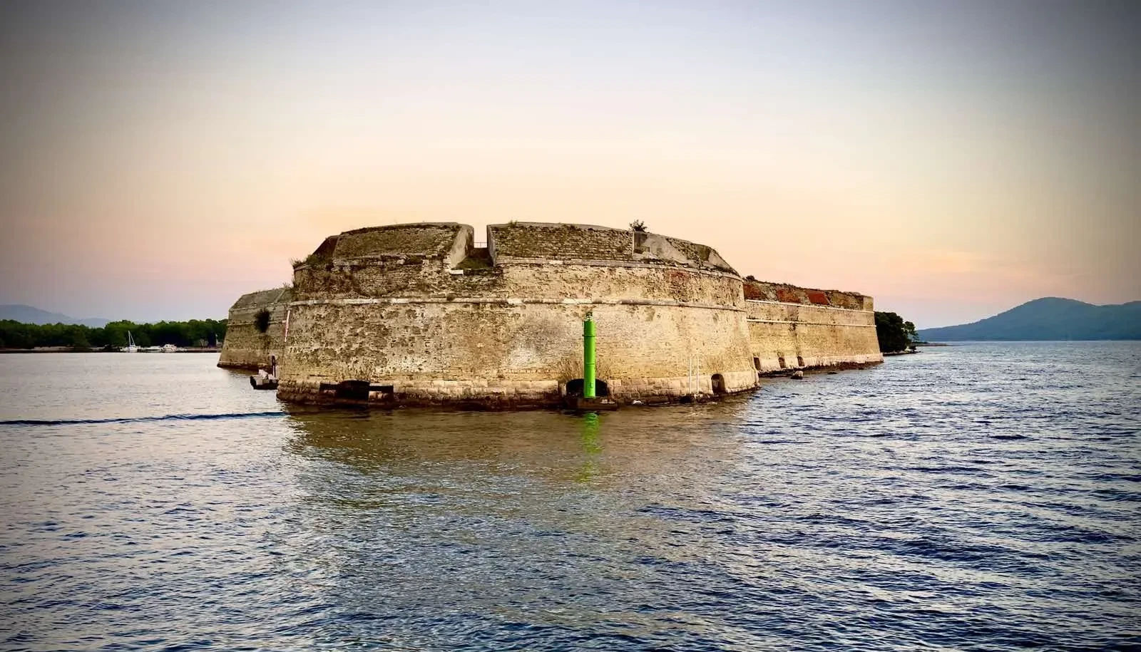 Historic sea fortress at dusk with weathered walls standing in calm waters against a soft sunset sky.